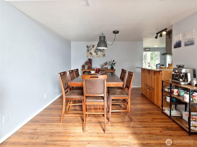 dining space featuring rail lighting, light wood-style flooring, and baseboards