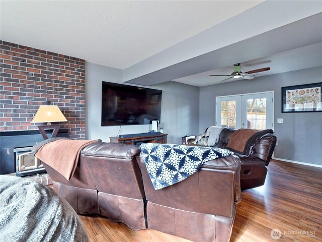 living room with a ceiling fan, wood finished floors, a wood stove, and baseboards