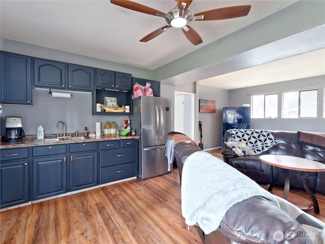 kitchen with freestanding refrigerator, open floor plan, a sink, wood finished floors, and blue cabinets