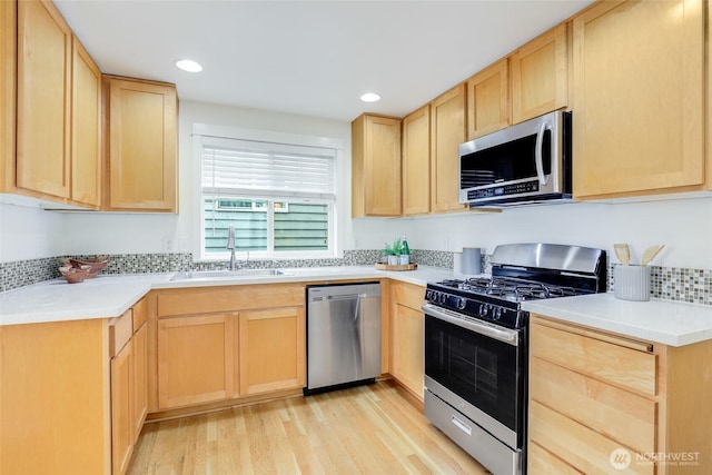 kitchen featuring stainless steel appliances, light countertops, a sink, and light brown cabinetry