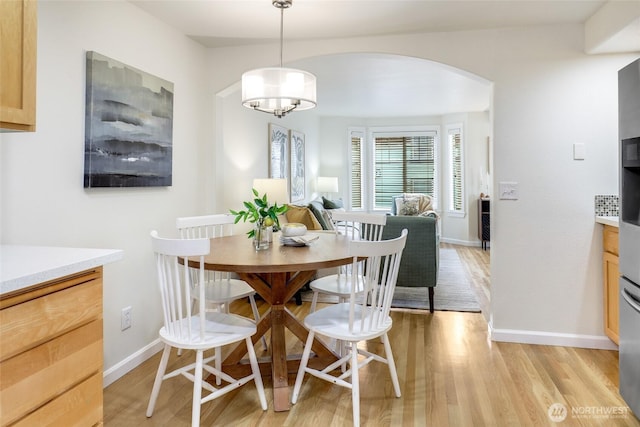 dining room with arched walkways, light wood finished floors, an inviting chandelier, and baseboards