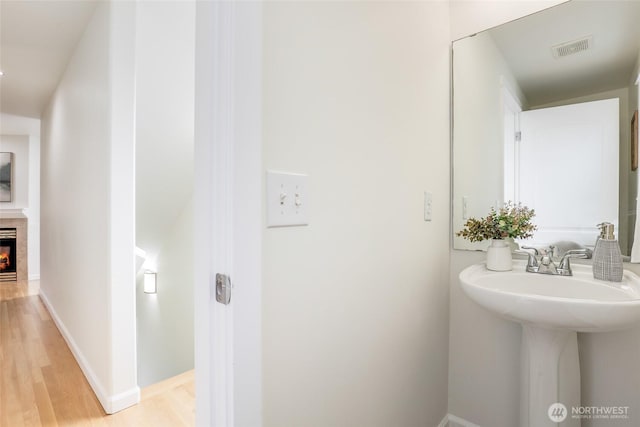 bathroom featuring baseboards, visible vents, a glass covered fireplace, wood finished floors, and a sink