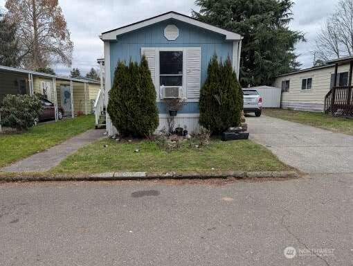 manufactured / mobile home featuring cooling unit, driveway, and a front lawn