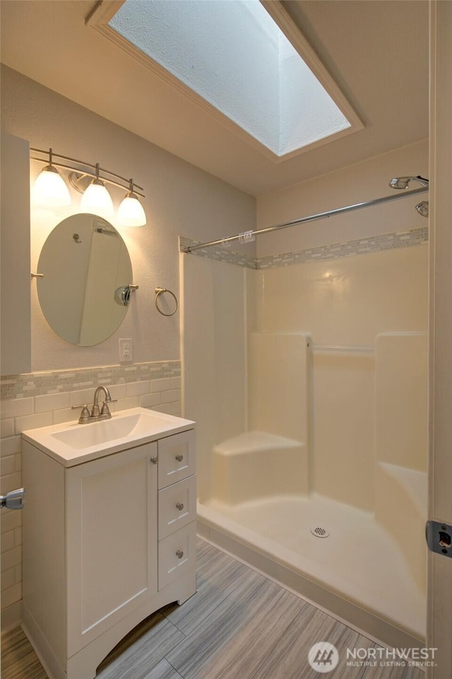 full bath featuring a shower, a skylight, a wainscoted wall, tile walls, and vanity