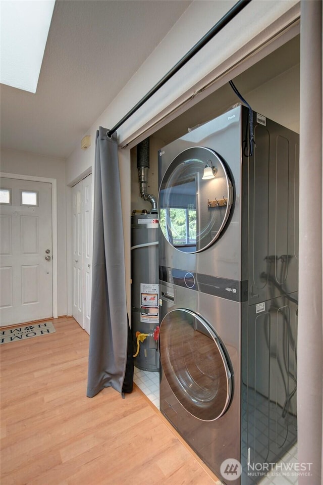 washroom featuring a skylight, strapped water heater, stacked washer / dryer, wood finished floors, and laundry area