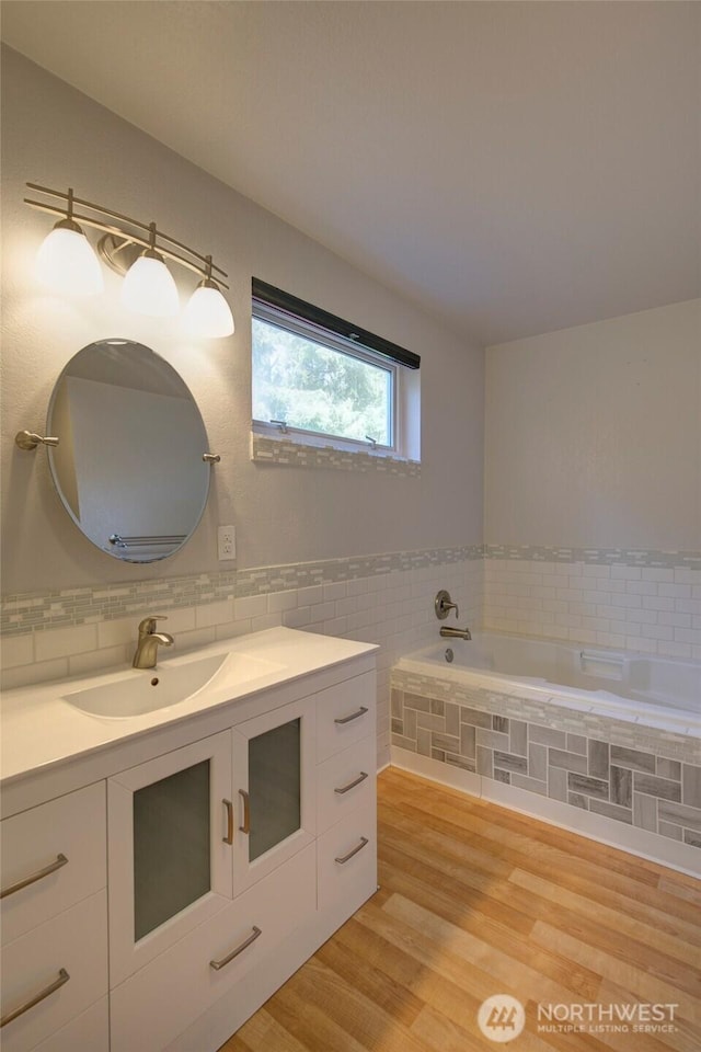 full bathroom with tile walls, vanity, a bath, and wood finished floors