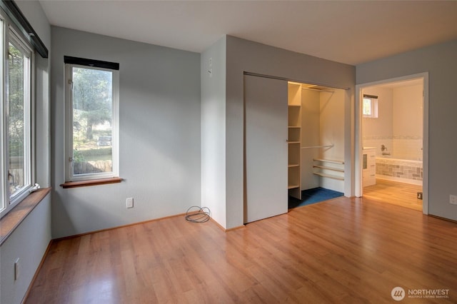 unfurnished bedroom featuring a closet, ensuite bath, and wood finished floors