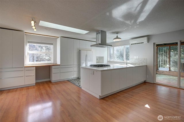 kitchen featuring island range hood, light wood-style flooring, a peninsula, an AC wall unit, and a sink