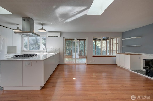 kitchen with a skylight, light wood finished floors, white cabinets, island exhaust hood, and a wall mounted AC