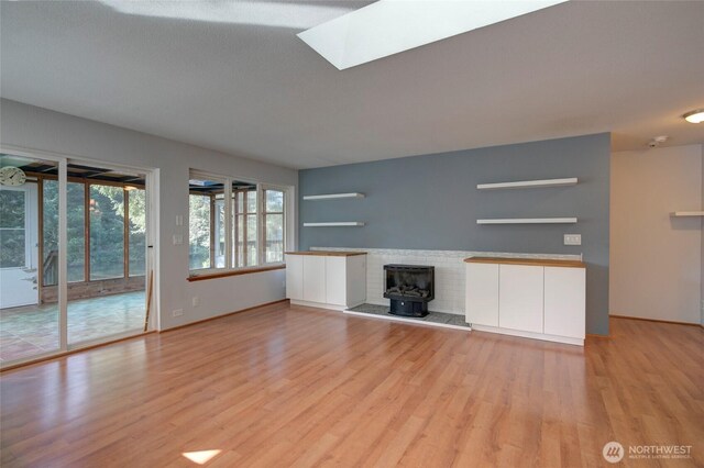 unfurnished living room with light wood-type flooring, a wood stove, and a skylight