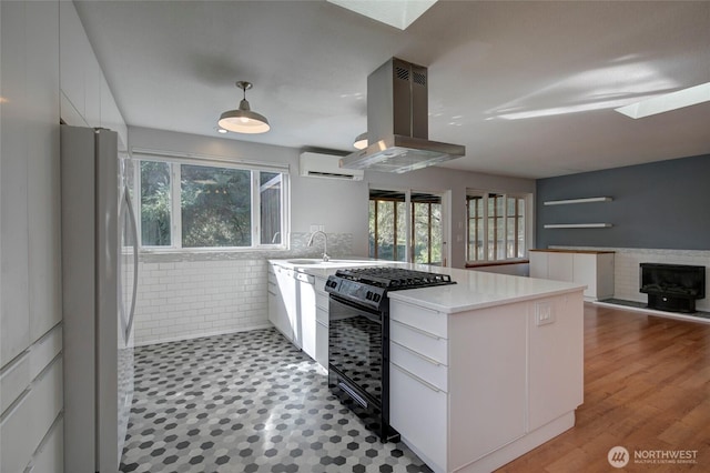 kitchen featuring black range with gas cooktop, island range hood, white cabinetry, an AC wall unit, and freestanding refrigerator