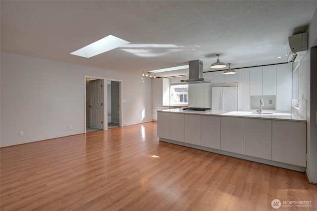 kitchen with extractor fan, light wood-style flooring, a peninsula, black cooktop, and freestanding refrigerator