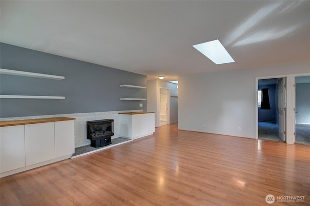 unfurnished living room featuring a wood stove, a skylight, and light wood-style flooring