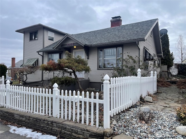 view of front of house with a fenced front yard, a chimney, and roof with shingles