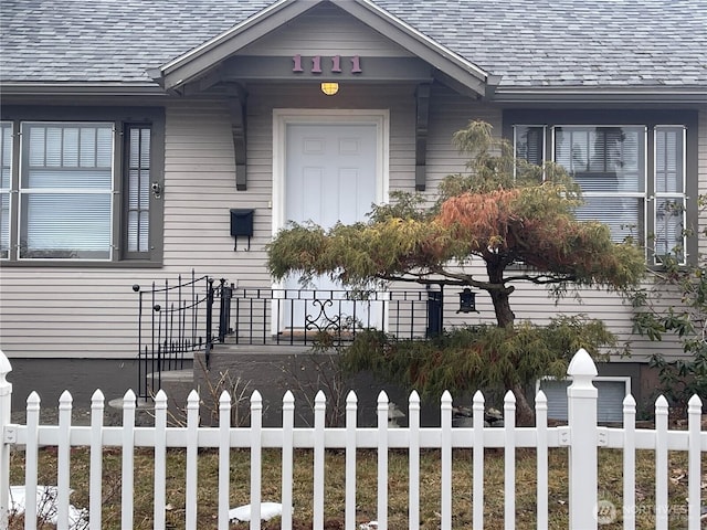 entrance to property featuring roof with shingles and fence