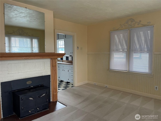 unfurnished living room with a textured ceiling, wainscoting, baseboards, and light colored carpet