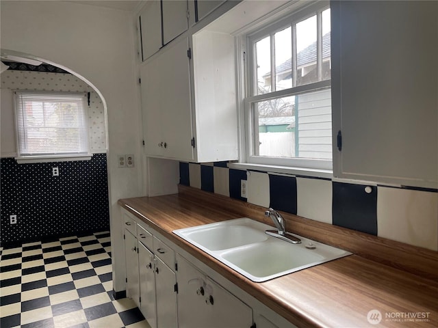 kitchen with light floors, a sink, wooden counters, and white cabinetry