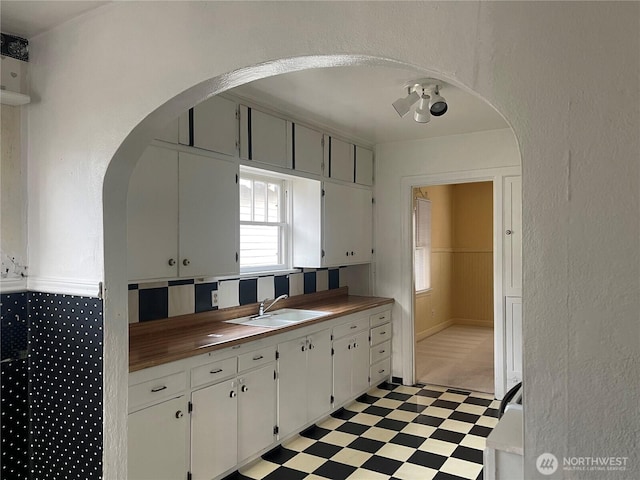 kitchen featuring arched walkways, a sink, light floors, and wooden counters