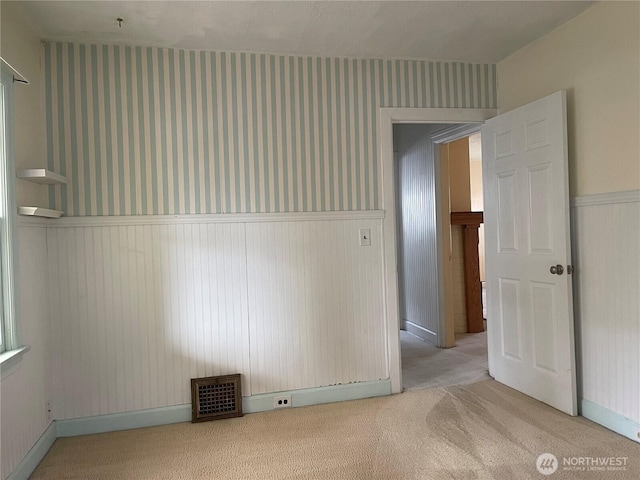 spare room featuring a wainscoted wall, visible vents, light carpet, and wallpapered walls