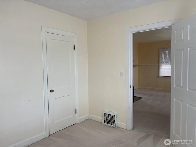 empty room featuring light carpet, a wainscoted wall, and visible vents