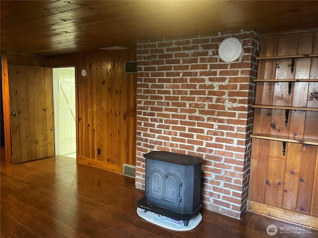 unfurnished living room with visible vents, wood walls, wood finished floors, and a wood stove