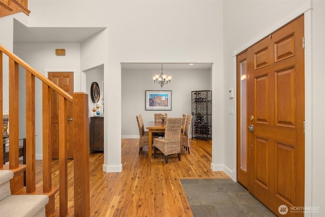 entryway featuring stairway, wood finished floors, baseboards, a high ceiling, and a notable chandelier