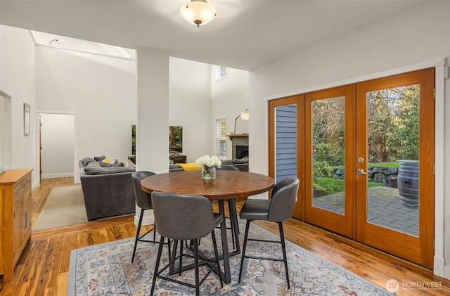 dining area featuring light wood-type flooring, a towering ceiling, a fireplace, and french doors