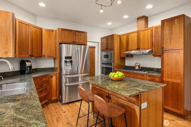 kitchen with under cabinet range hood, light wood-type flooring, a kitchen breakfast bar, stainless steel appliances, and a sink