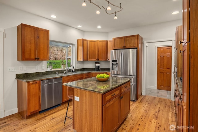 kitchen with a sink, appliances with stainless steel finishes, light wood-style flooring, and brown cabinetry