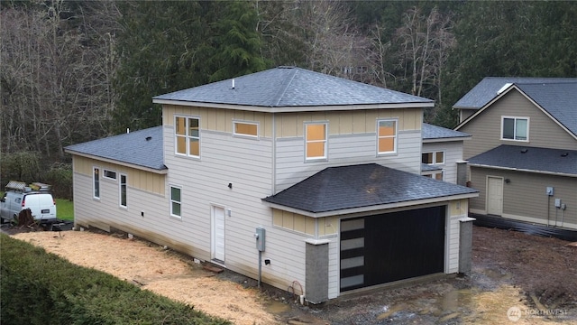 rear view of property featuring a view of trees, roof with shingles, and board and batten siding