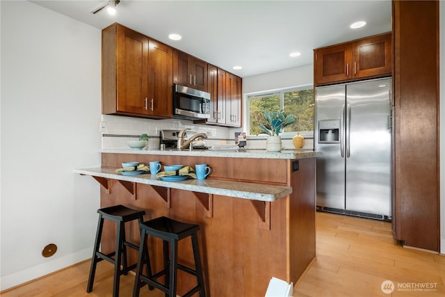 kitchen featuring light wood finished floors, a peninsula, appliances with stainless steel finishes, and backsplash