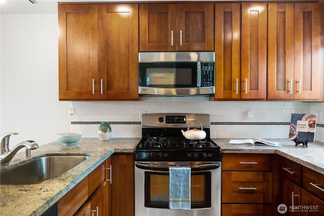 kitchen with light stone countertops, tasteful backsplash, appliances with stainless steel finishes, and a sink