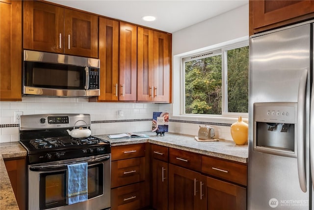 kitchen with appliances with stainless steel finishes, brown cabinets, backsplash, and light stone counters