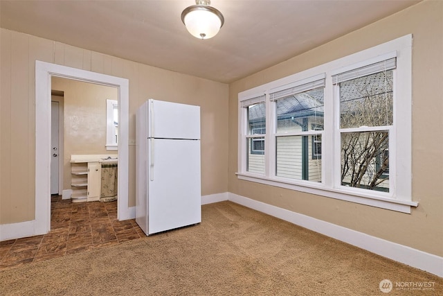 unfurnished bedroom featuring freestanding refrigerator, dark carpet, wooden walls, and baseboards