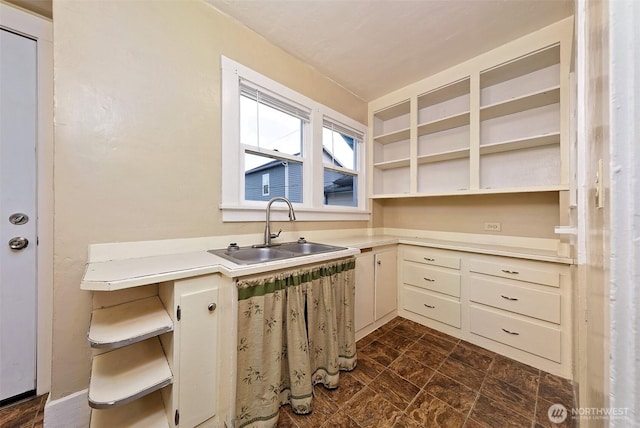 kitchen with stone finish floor, a breakfast bar, light countertops, open shelves, and a sink