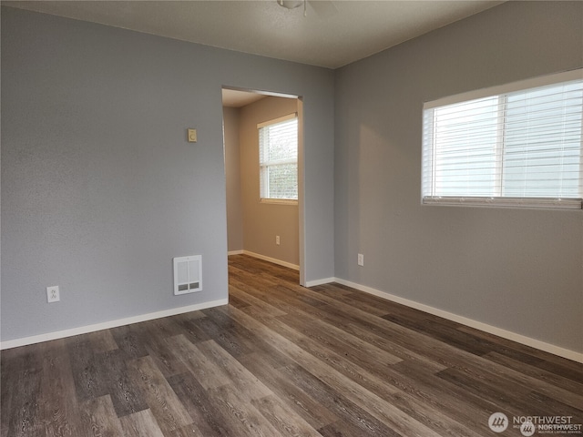 empty room with dark wood-style floors, visible vents, and baseboards