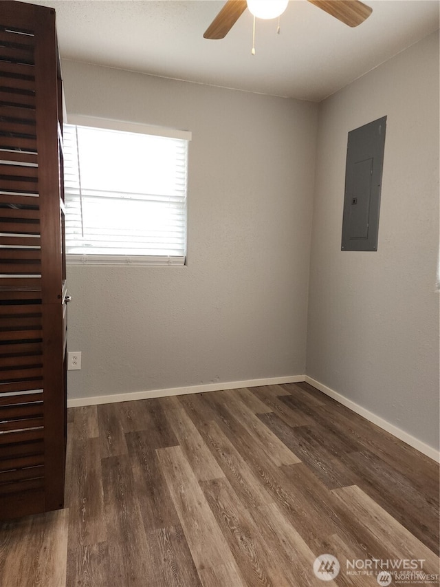 unfurnished room with dark wood-style flooring, electric panel, ceiling fan, and baseboards