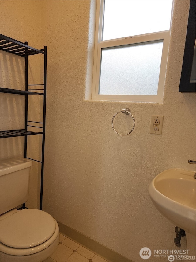 half bath featuring tile patterned flooring, baseboards, a sink, and toilet