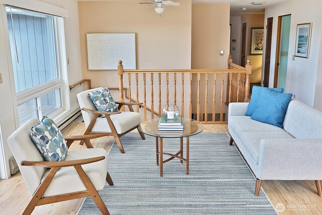 sitting room with a baseboard radiator, an upstairs landing, wood finished floors, and a ceiling fan