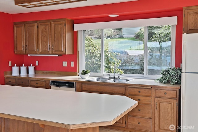 kitchen featuring white appliances, light countertops, brown cabinets, and a sink