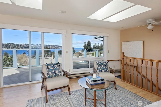 sitting room featuring light wood-style flooring, a water view, and a skylight