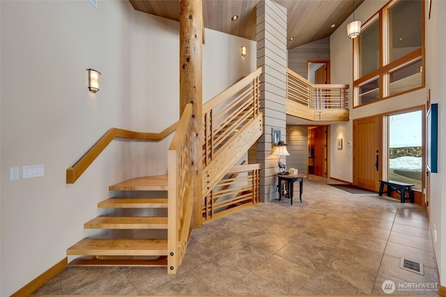 staircase with a high ceiling, wood walls, wood ceiling, visible vents, and baseboards