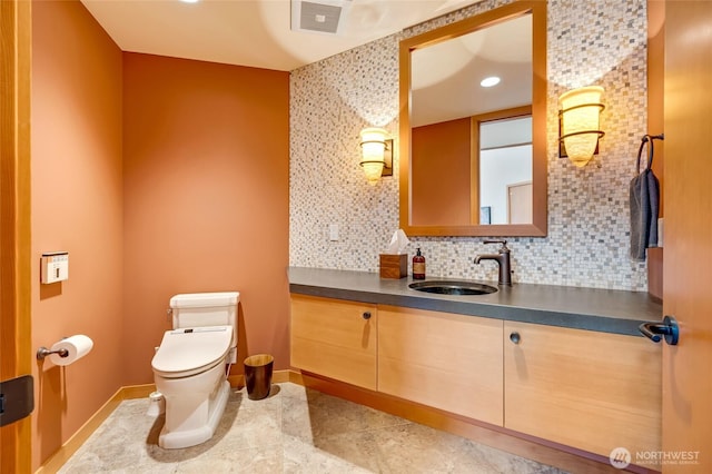 half bath featuring baseboards, visible vents, decorative backsplash, toilet, and vanity