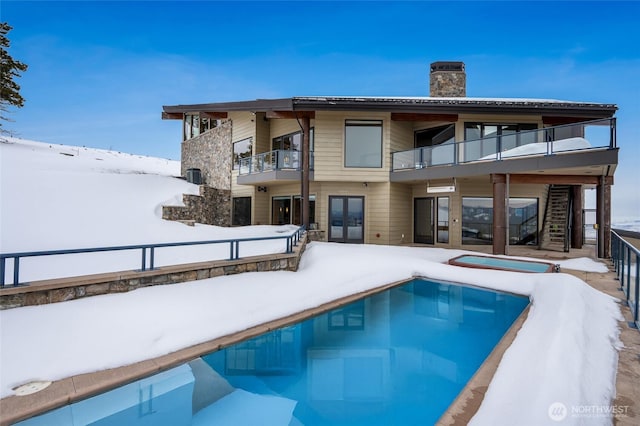 snow covered property featuring french doors, a chimney, a balcony, and an outdoor pool