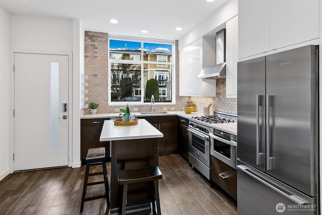 kitchen featuring a kitchen island, light countertops, wall chimney range hood, high end appliances, and modern cabinets