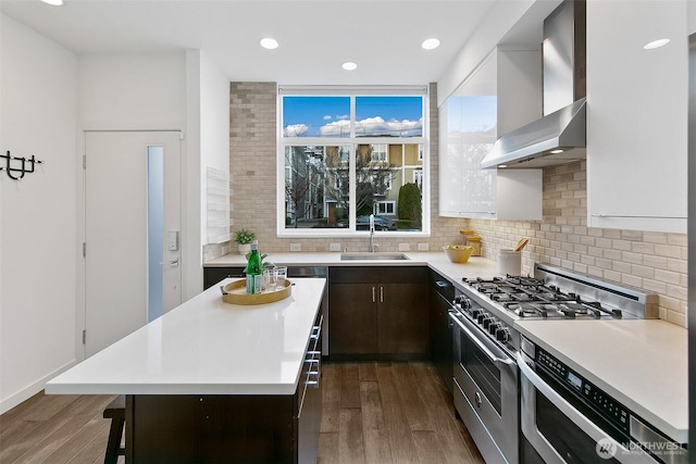 kitchen featuring a breakfast bar, stainless steel range, light countertops, a sink, and wall chimney exhaust hood