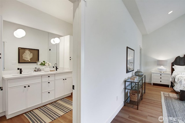 bedroom featuring a sink, light wood-type flooring, baseboards, and ensuite bathroom