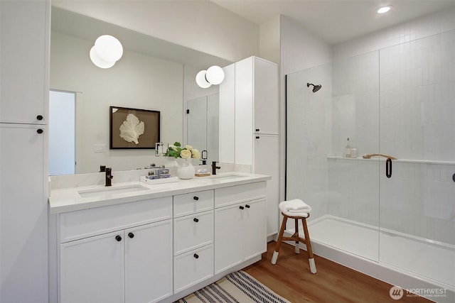 full bath featuring a tile shower, wood finished floors, and a sink