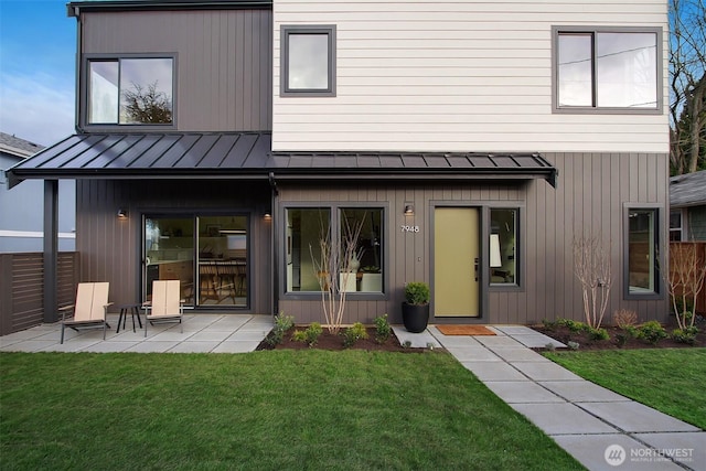 back of house with fence, a standing seam roof, a patio area, a lawn, and metal roof