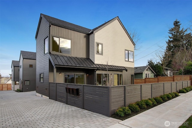 back of house with a fenced front yard, board and batten siding, metal roof, and a standing seam roof